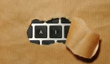 Torn brown packing paper pulled back to reveal keyboard keys spelling AI